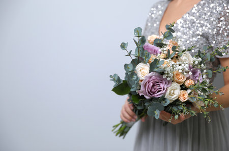 Bride holding beautiful wedding bouquet on light grey background, closeup. Space for textの写真素材