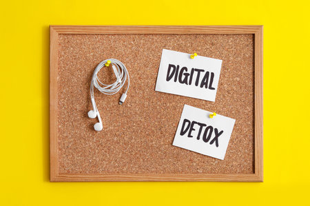 Corkboard with words DIGITAL DETOX and earphones hanging on yellow backgroundの写真素材