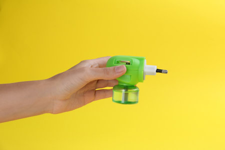 Woman holding electric vaporizer with insect repellent liquid on yellow background, closeupの写真素材