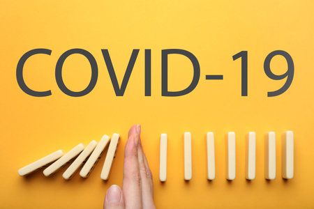 Woman stopping domino effect on yellow background, top view. Prevent the spread of coronavirusの写真素材