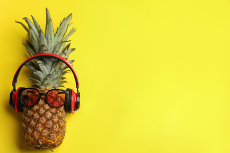 Top view of pineapple with sunglasses and headphones on yellow background, space for text. creative conceptの写真素材
