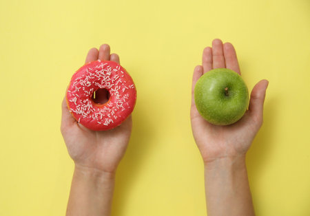 Top view of woman choosing between donut and healthy apple on yellow background, closeupの写真素材