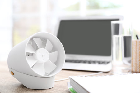 Modern portable fan on wooden table in office, space for text. summer heat
