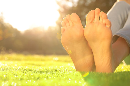 Young woman sitting barefoot on fresh green grass outdoors, closeupの写真素材