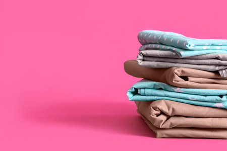 Stack of clean bed sheets on pink background. Space for textの写真素材