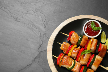 Delicious chicken shish kebabs with vegetables and sauce on gray table, top view. Space for textの写真素材