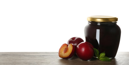 Glass jar of pickled plums on wooden table against white background, space for textの写真素材