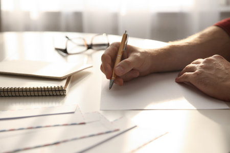 Man writing letter at white table in room, closeupの写真素材