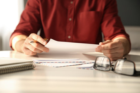 Man writing letter at white table in room, closeupの写真素材