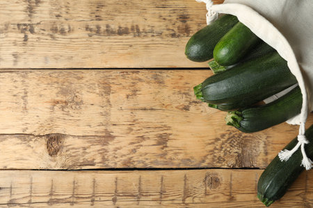 Sack with green ripe zucchinis on wooden table, flat lay. Space for textの写真素材