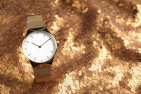Luxury wrist watch on gold paillette background. Space for text