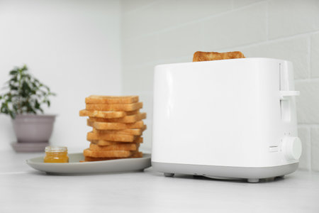 Modern toaster with slices of bread and honey on white table in kitchenの写真素材