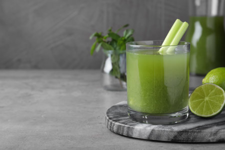Glass of fresh celery juice and lime on gray table, closeup. Space for textの写真素材