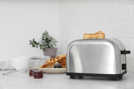 Modern toaster with slices of bread and different jams on white table in kitchenの写真素材