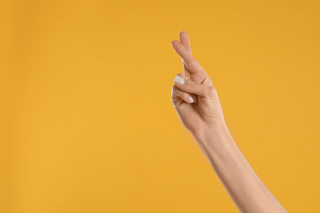Woman with crossed fingers and space for text on yellow background, closeup. superstition conceptの写真素材