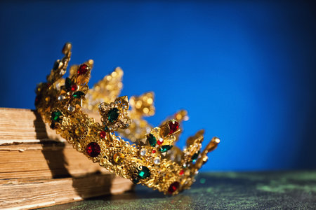 Beautiful golden crown and old books on dark blue background, space for text. fantasy itemの写真素材