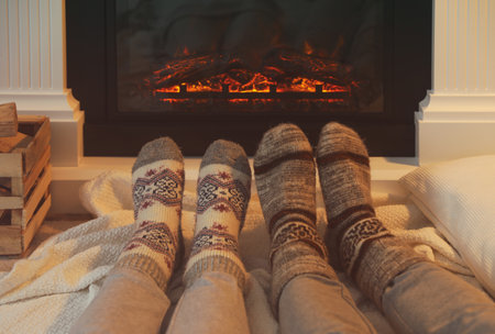 Couple in warm socks resting near fireplace at home, closeupの写真素材