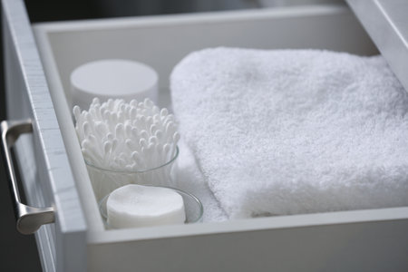 Open cabinet drawer with cotton buds, pads and towels indoors, closeupの写真素材