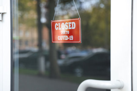 Red sign with words "Closed Due To Covid-19" hanging on glass doorの写真素材