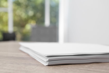 Stack of blank paper sheets on wooden table in office, closeup