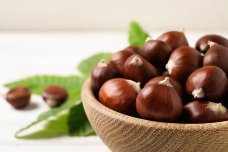 Fresh sweet edible chestnuts in bowl on white table, closeupの写真素材