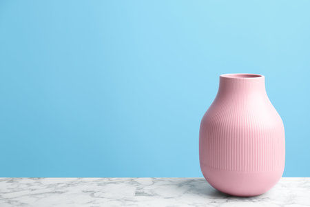 Stylish pink ceramic vase on white marble table against light blue background, space for textの写真素材