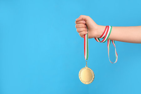 Woman holding gold medal on light blue background, closeup. Space for textの写真素材