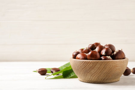 Fresh sweet edible chestnuts in bowl on white wooden table. Space for textの写真素材