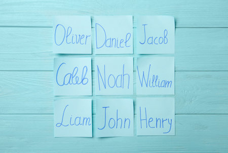 Paper notes with different baby names on light blue wooden table, flat layの写真素材