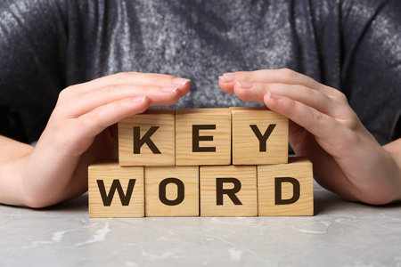 Woman demonstrating cubes with word KEYWORD at grey marble table, closeupの写真素材