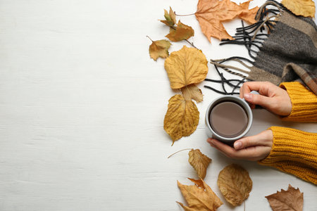 Woman with cup of hot drink at white wooden table, top view with space for text. Cozy autumn atmosphereの写真素材