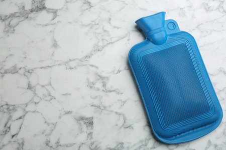Blue rubber hot water bottle on white marble background, top view. Space for textの写真素材