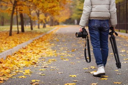 Photographer with professional camera and tripod outdoors on autumn day, closeup. Space for textの写真素材
