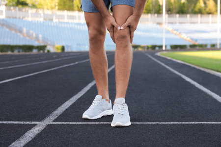 Man in sportswear having knee problems at stadium, closeupの写真素材