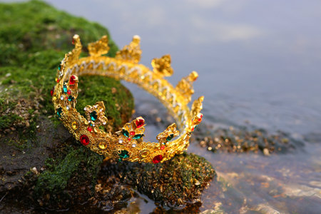 Beautiful golden crown on stone with green moss near river outdoors, closeup. fantasy itemの写真素材
