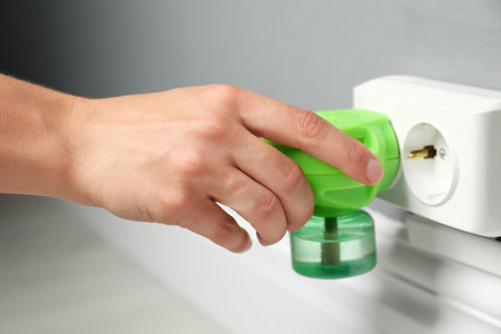 Woman plugging electric vaporizer with insect repellent liquid at home, closeup