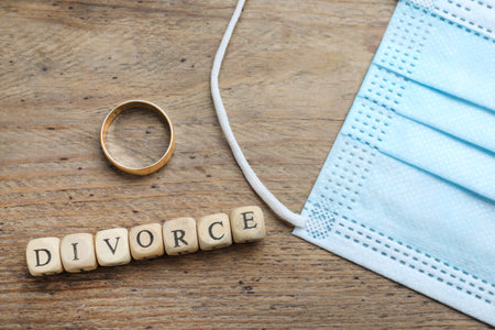 Flat lay composition with protective mask and wedding ring on wooden table. Divorce during pandemicの写真素材