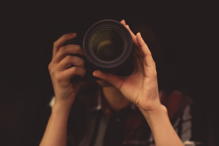Private detective with camera spying against black background, focus on lensの写真素材