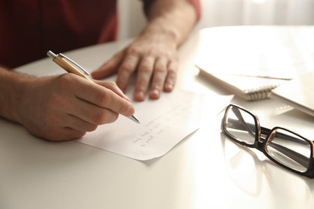 Man writing letter at white table in room, closeupの写真素材