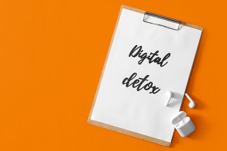 Clipboard with words DIGITAL DETOX and earphones on orange background, flat lay. Space for textの写真素材