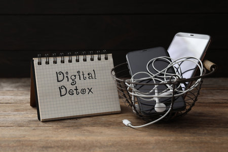 Trash bin with different gadgets and words DIGITAL DETOX on wooden tableの写真素材