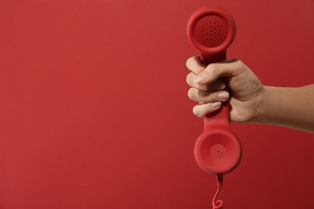Closeup view of woman holding corded telephone handset on red background, space for text. hotline conceptの写真素材