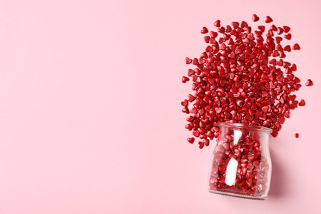 Red heart shaped sprinkles and glass jar on pink background, flat lay. Space for textの写真素材