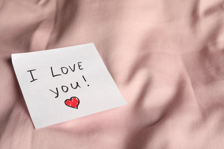 Sticky note with phrase I love you! on bed, close up. Space for textの写真素材