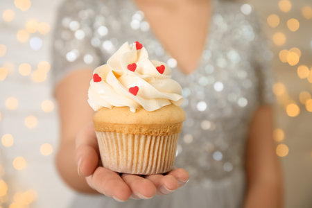 Woman holding tasty cupcake for Valentine's Day against blurred lights, closeupの写真素材