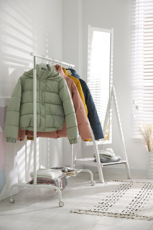 Different warm jackets on rack in stylish room interiorの写真素材