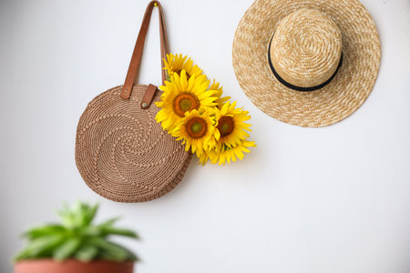 Knitted bag with bouquet of beautiful sunflowers and straw hat on white wallの写真素材