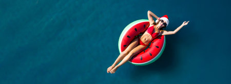 Young woman wearing Santa hat and swimsuit with inflatable ring in sea, top view. christmas holidaysの写真素材