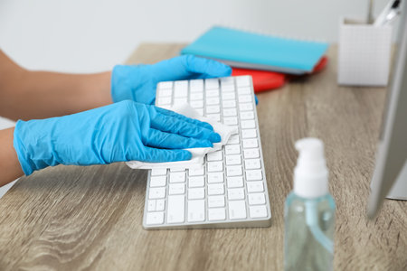 Woman cleaning computer keyboard with antiseptic wipe in office, closeupの写真素材