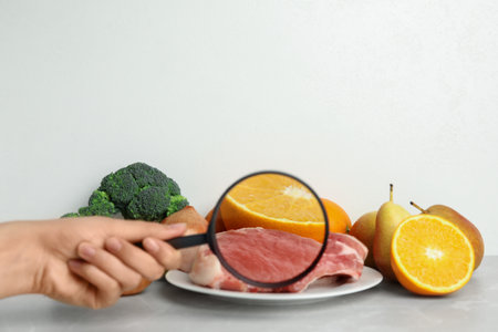 Woman with magnifying glass exploring raw meat and fruits, space for text. Poison detectionの写真素材